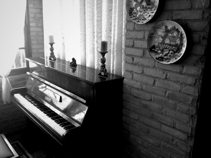 Monochrome photograph of an upright piano with candles and decorative plates