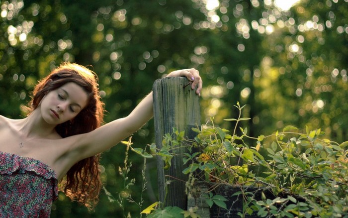 Woman in floral dress leaning on wooden post in sunlight