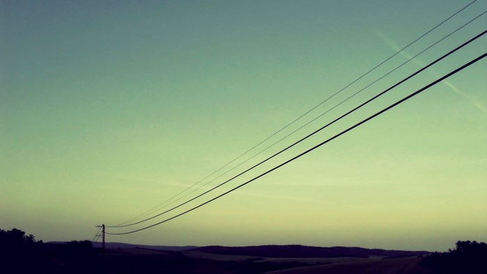 Power lines against a gradient sky over rolling hills
