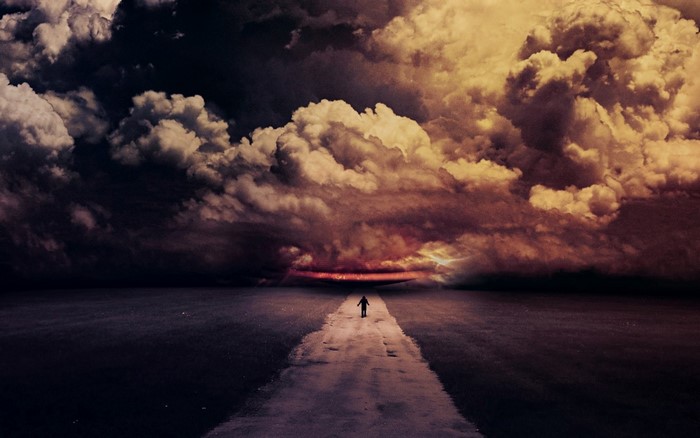 Person walking on a road towards a stormy sunset over the sea