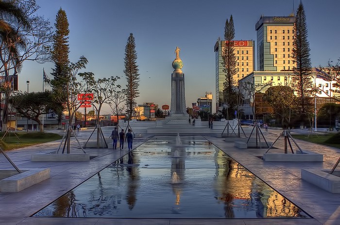 Monument with globe and statue in a city plaza with fountains