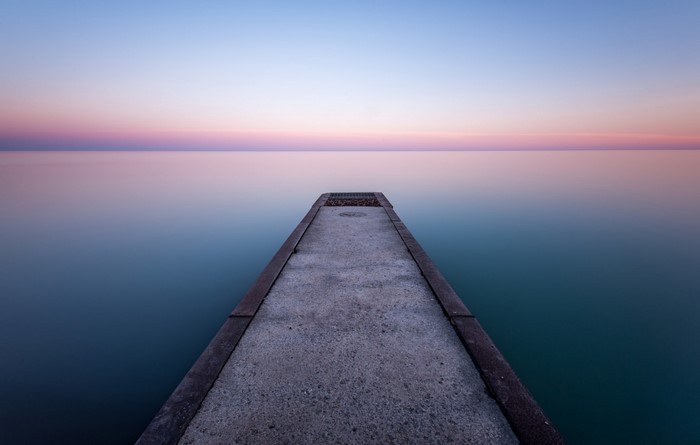 Concrete pier extending into calm ocean at sunset