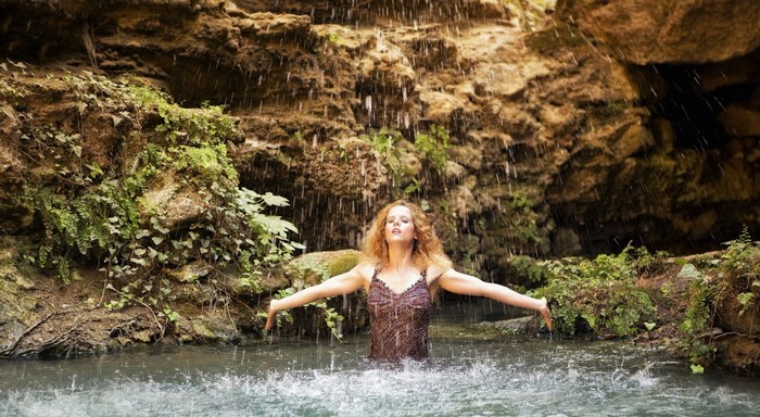 Woman standing in water under a waterfall in a cave