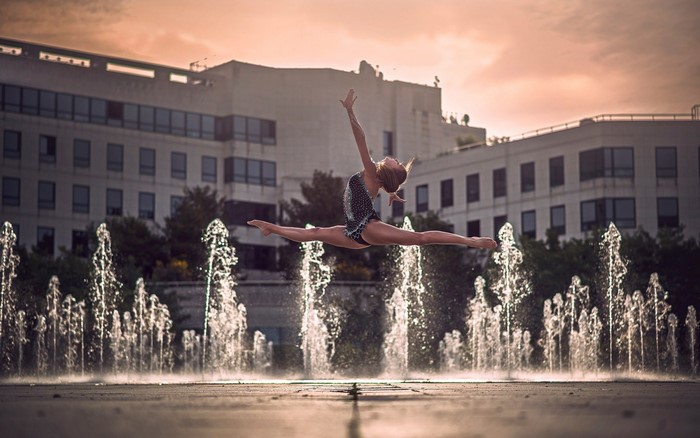 Woman performing a split jump in front of fountains and buildings