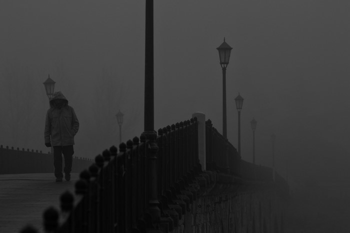 Person walking on a foggy bridge with street lights