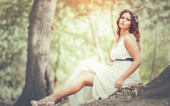 Woman with flower crown in a white dress sitting in a forest