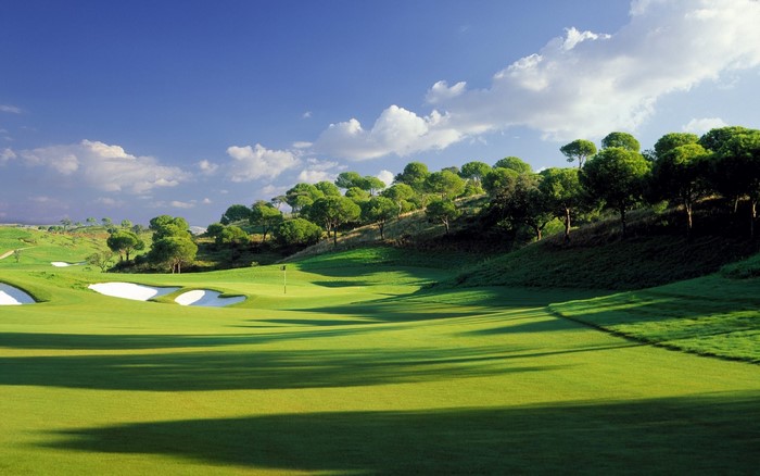 Golf course with sand traps and trees under a blue sky