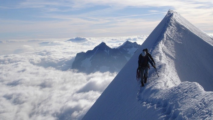 Mountaineers climbing a snowy ridge above clouds in the Alps