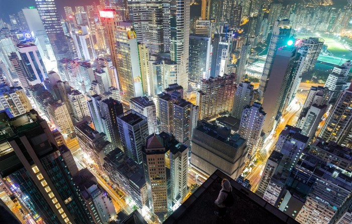 Person on skyscraper rooftop overlooking city skyline at night