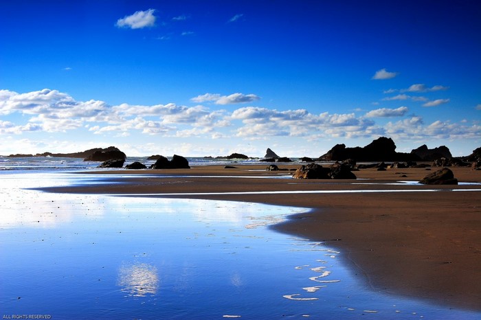 Beach with rocks and reflection under blue sky