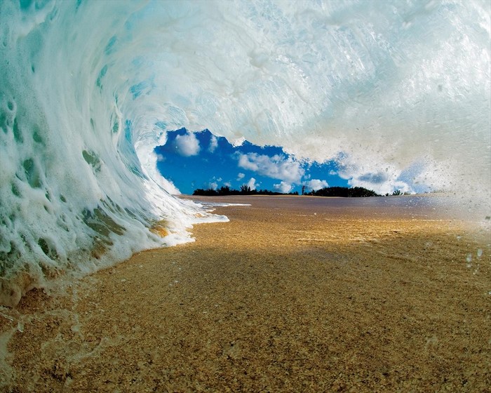 Wave crashing on a sandy beach with blue sky