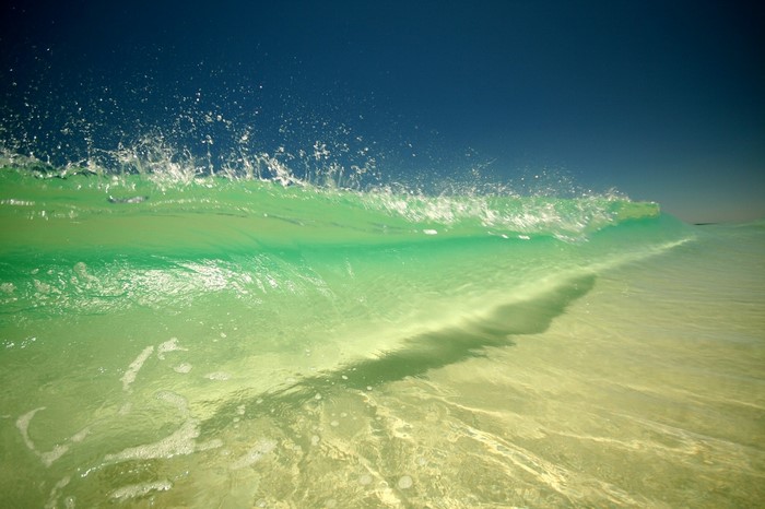 Green wave crashing under a clear blue sky