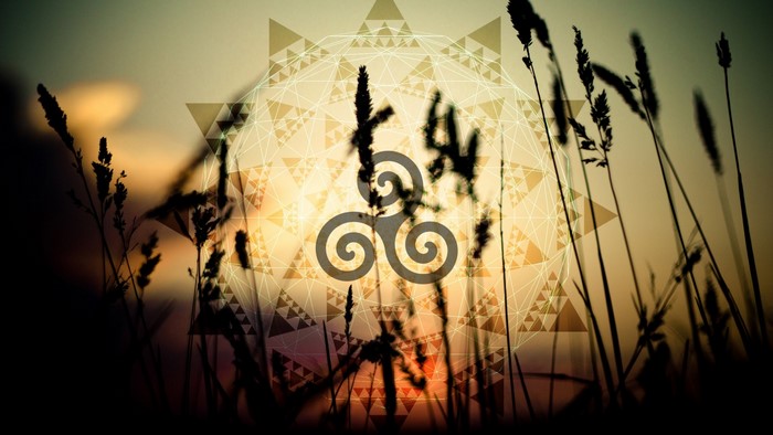 Triskelion symbol over sunset with grass silhouettes