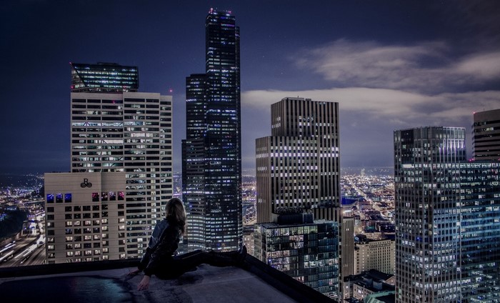 Woman on rooftop overlooking city skyline at night