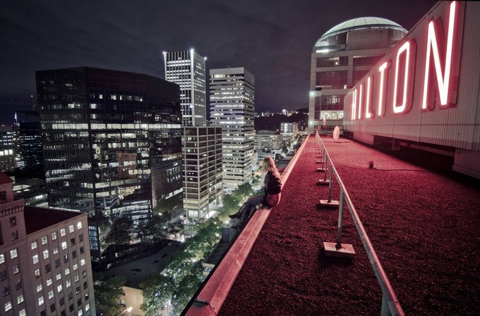 Woman sitting on a rooftop overlooking a city at night