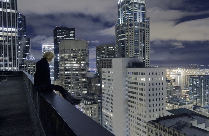 Woman sitting on a rooftop overlooking a city skyline at night