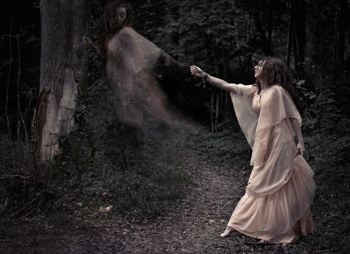 Woman reaching for a ghost in a dark forest