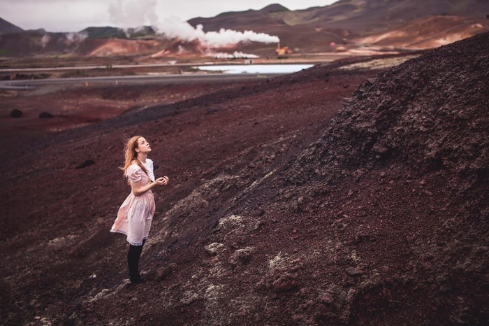 Woman in pink dress on volcanic terrain with geothermal activity