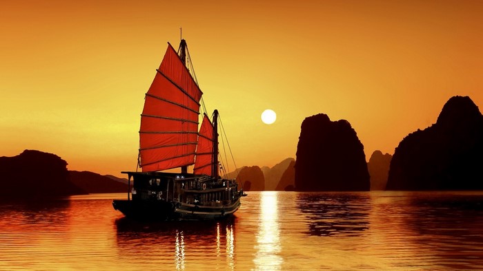 Junk boat sailing at sunset in a bay with karst formations