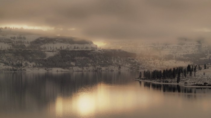 Misty winter landscape with snow-covered hills and lake reflection