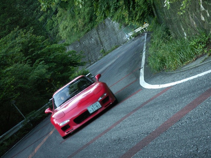 Red Mazda RX-7 driving on a winding mountain road