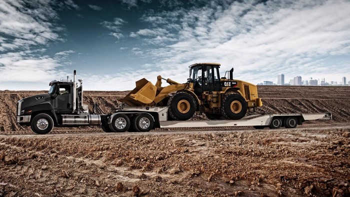Black semi-truck hauling a yellow CAT wheel loader on a trailer