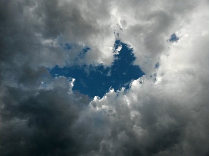 A hole in dark storm clouds reveals a bright blue sky