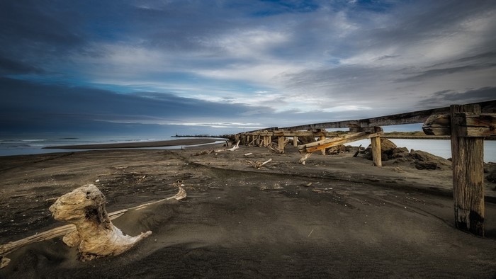 Wooden pier ruins on a sandy beach at dusk