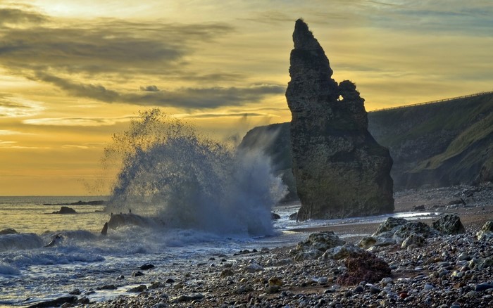 Wave crashing on a rocky shore at sunset