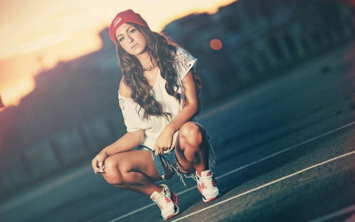 Woman in red beanie and denim shorts crouching outdoors