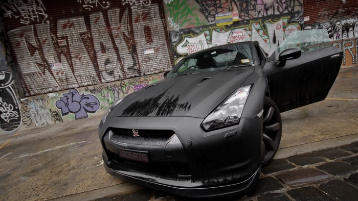 Matte black Nissan GT-R with open door in graffiti alley