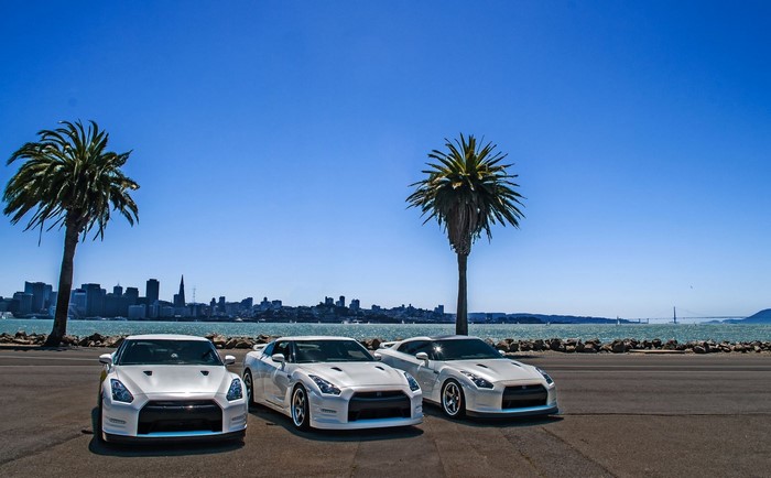 Three white Nissan GT-R cars parked by the water with San Francisco skyline
