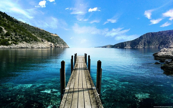 Wooden pier extending into a clear blue sea with mountains