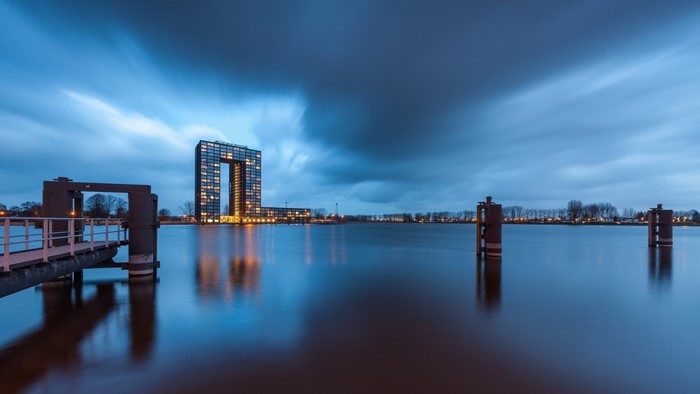 Modern building with archway reflected in water at dusk