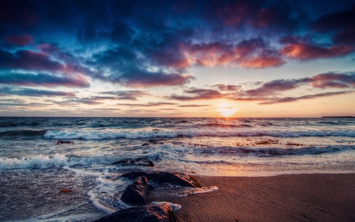 Sunset over the ocean with waves crashing on the shore
