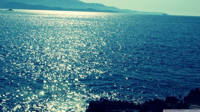 Sparkling sea with distant mountains and rocky shore