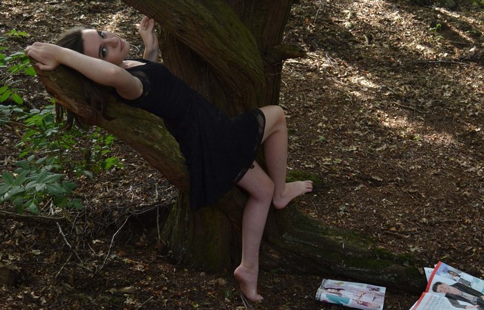 Woman in black dress posing on a tree in a forest