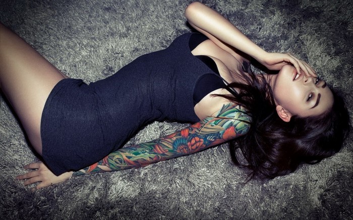 Woman with full sleeve tattoo lying on carpet