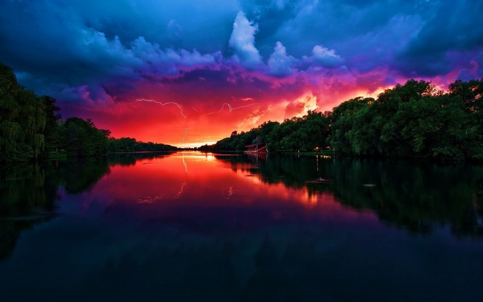 Lightning strikes over a lake at sunset with colorful clouds