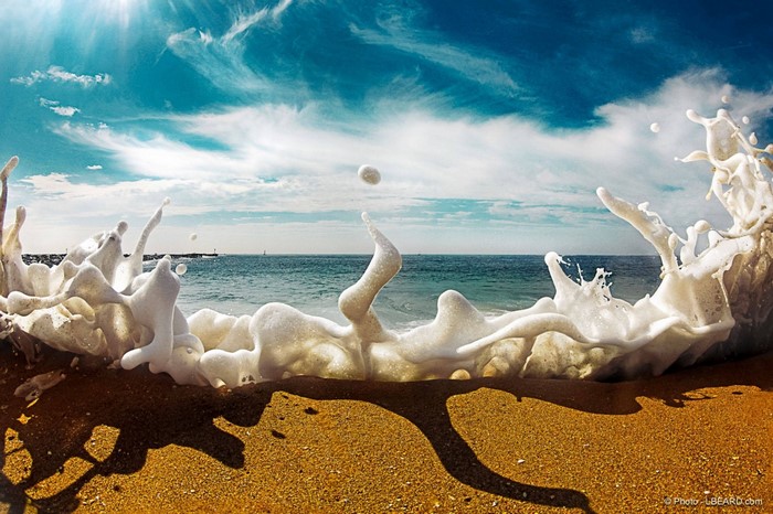 Wave crashing on a sandy beach with blue sky and clouds