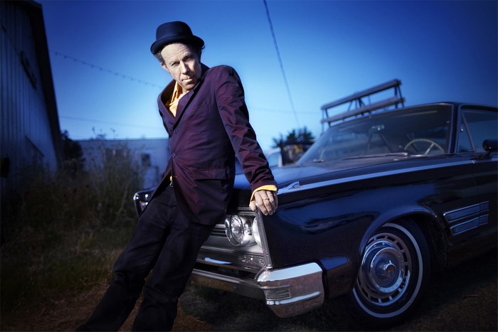 Tom Waits leaning on a vintage car