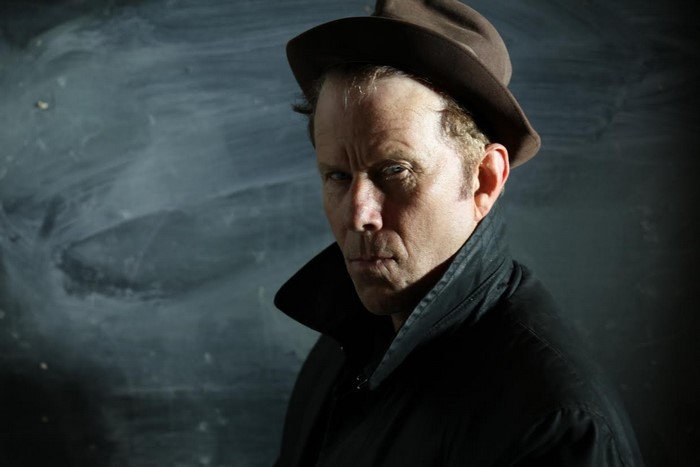 Tom Waits wearing a hat and trench coat