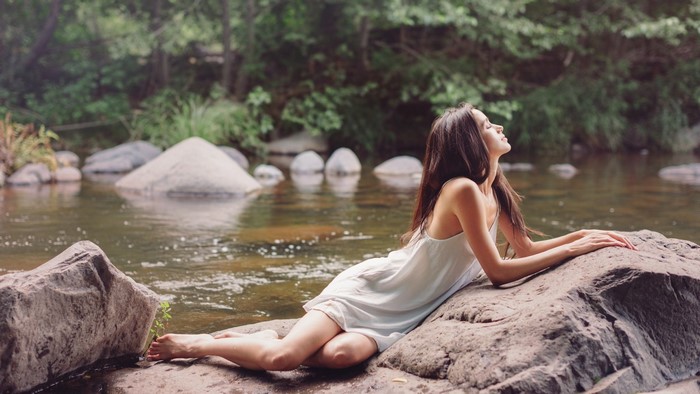 Woman in white dress lying on rocks by river