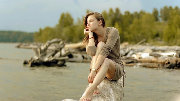 Thoughtful Woman Sitting on a Log by the Water