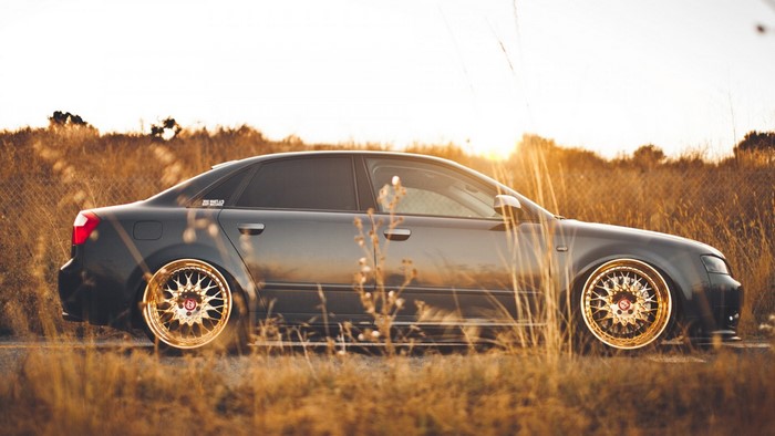 Dark gray Audi sedan with gold rims parked in dry grass