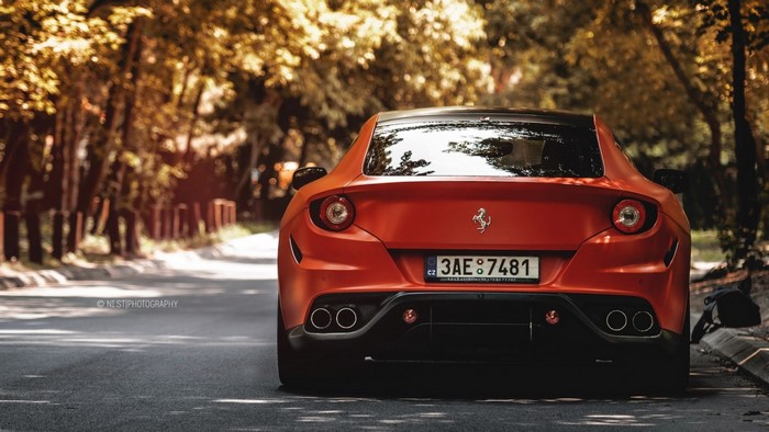 Red Ferrari F12berlinetta parked on a tree-lined road
