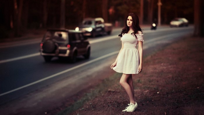 Woman in a white dress standing by a road