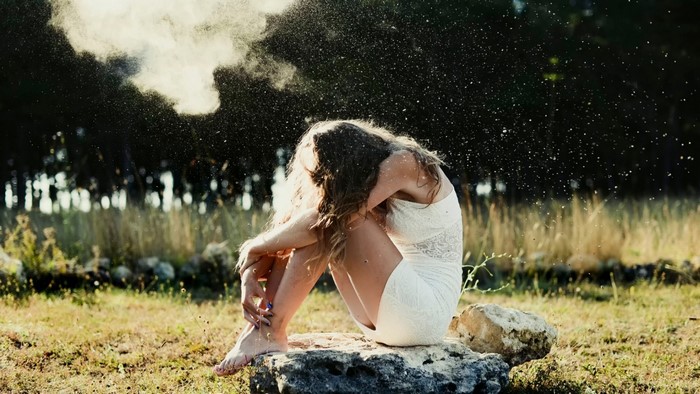 Woman in white dress sitting on rock with dust in air