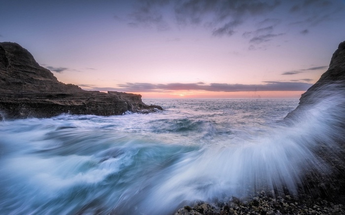 Waves crashing against rocky cliffs at sunset