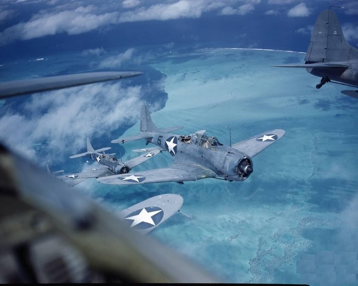 Douglas SBD Dauntless aircraft in flight over turquoise water